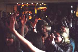 AN image of a crowd in a dark room - everyone is waving thier hands in the air - the image is slightly blurred showing the movement of bodies