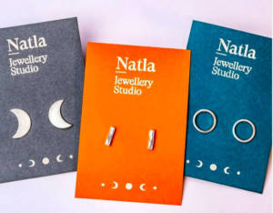 Three sets of silver earrings on colourful card, they each are silver crescent moons, small bar and circle shaped studs